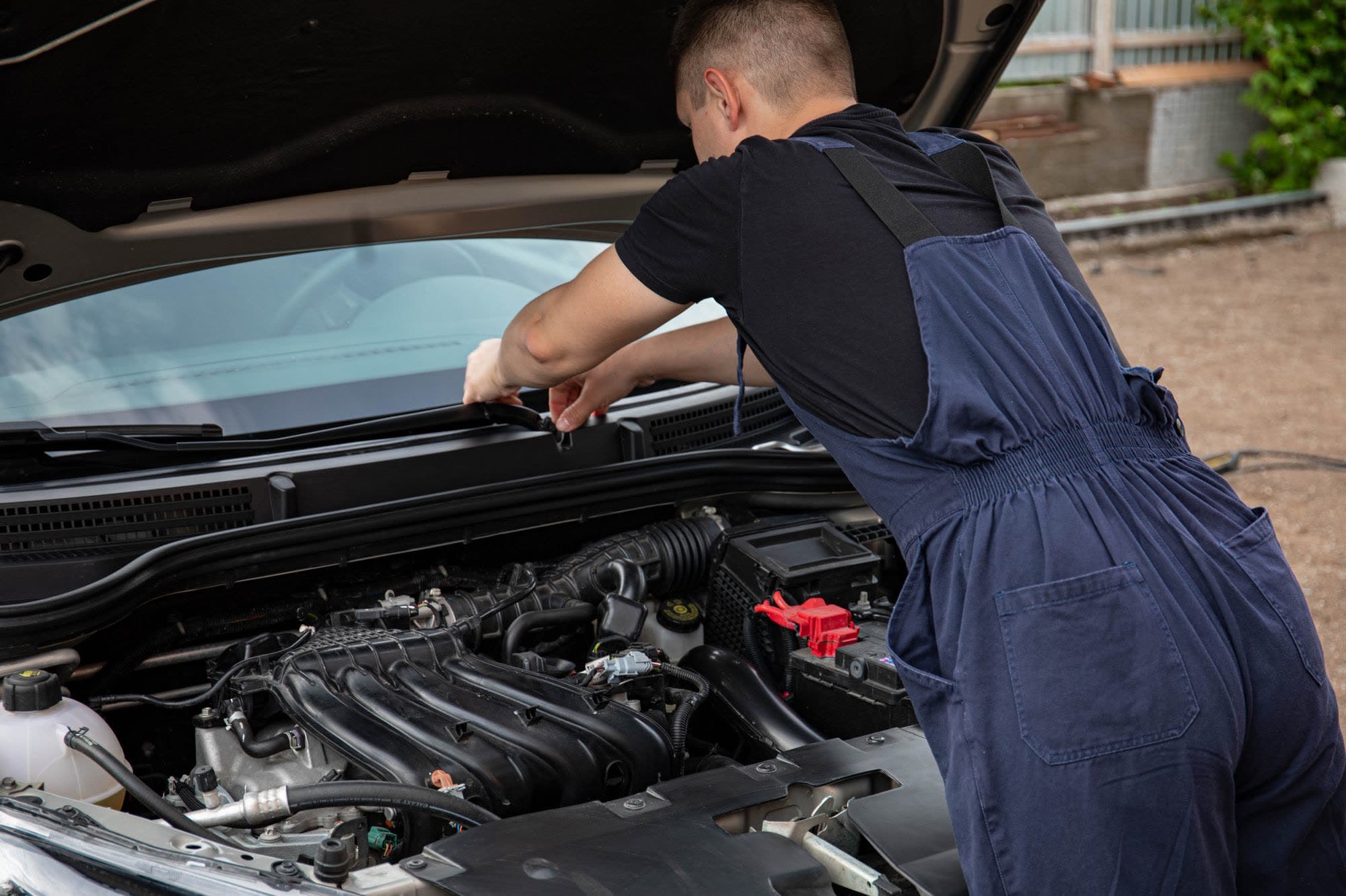 Mobile mechanic working under the open hood of a car at a customer's home