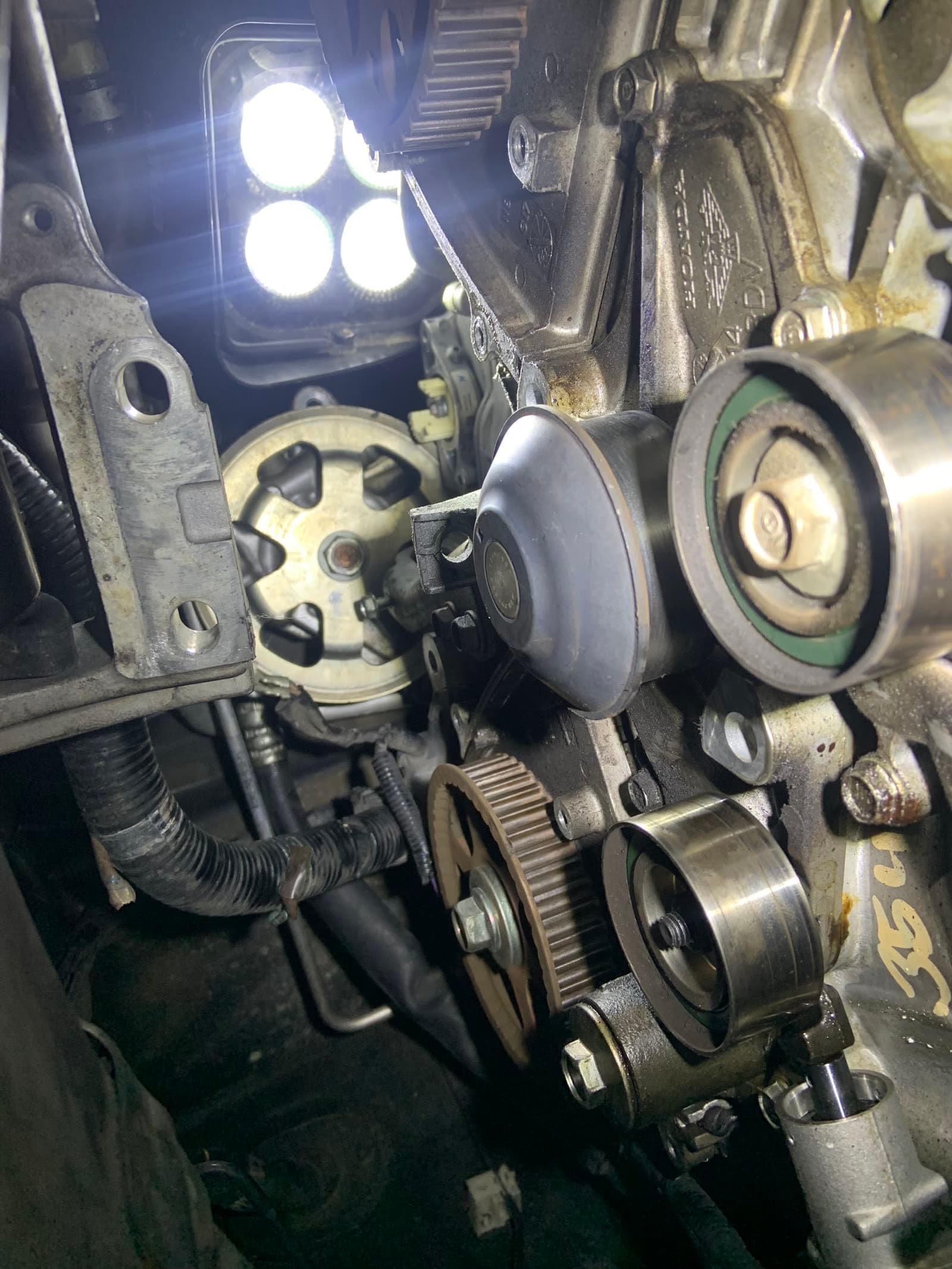 Timing belt, tensioner and cam pulleys exposed on a Honda engine, lit by a work light — one of Jay's own jobs