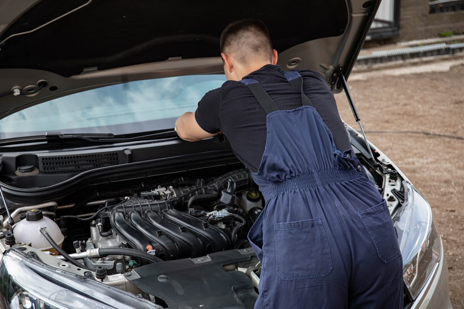 A mechanic working under an open hood outdoors, away from any shop